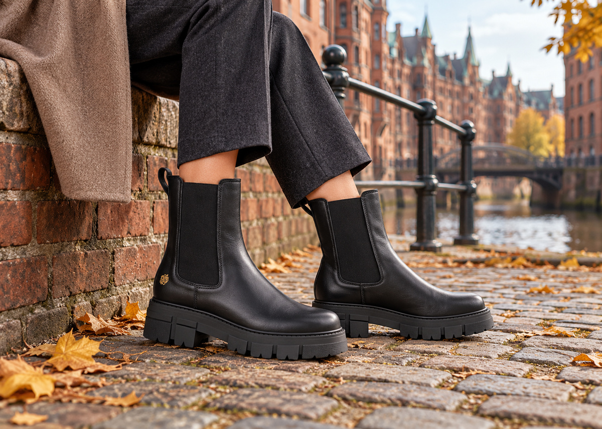 Schwarze Chelsea-Boots im herbstlichen Hafenmotiv